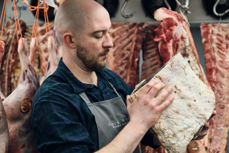 A butcher inspects a cut of meat in chilled storage room at Ruby & White butchers in Clifton, Bristol